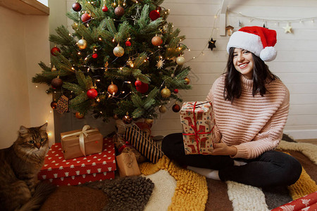 时尚的年轻女子拿着红色圣诞礼盒在圣诞树下图片