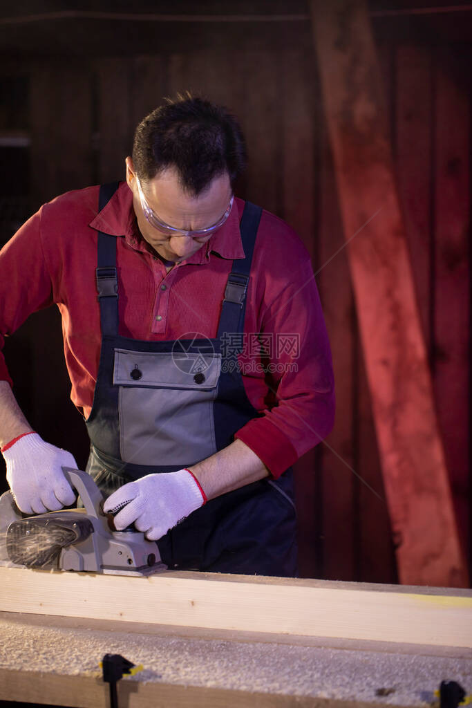 中年男工匠木在乡间别墅车间的工作台上用电动刨床加工件木工在木头上工作在乡间别墅工作图片
