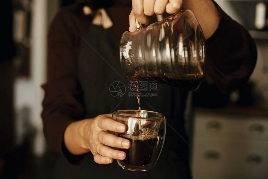 身着黑色制服的专业女咖啡师制作滴滤咖啡人从杯子里的玻璃水壶里倒出新鲜的芳香咖啡替代咖啡图片