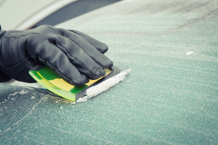 黑手套人手用刮刀把车窗上的冰或雪从车窗中除去图片