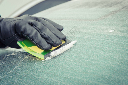 黑手套人手用刮刀把车窗上的冰或雪从车窗中除去图片