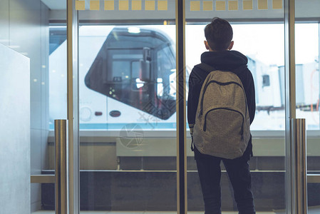 一个背着包的男孩站在机场的玻璃门附近图片