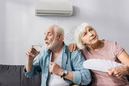 家中沙发上饮用水的老年妇女在丈夫身边抱着风图片
