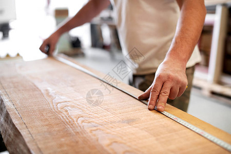 木匠在车间用卷尺测量一块木板的长度图片