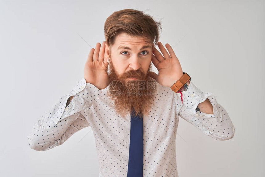 年轻的红发爱尔兰商人站在孤立的白色背景上试图听到双手放在耳朵上的手势图片
