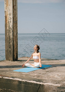 在海边练习瑜伽的女人坐在莲花姿势图片