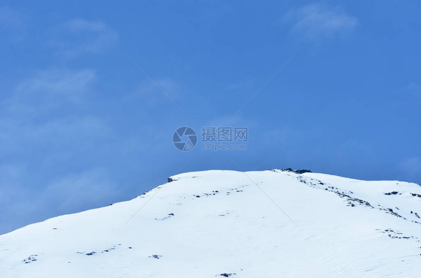 富士山的圆锥体在湛蓝的天空中升起一些薄雾从山的一侧吹过在前景中可以看到几棵树的顶部在一侧可以看图片