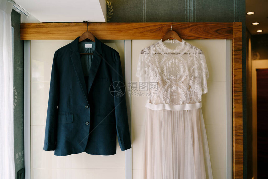 新娘结婚礼服和新郎夹克挂在木衣架上图片