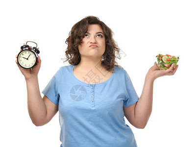 带着沙拉碗和闹钟在白色背景上挂着的超重不高兴的女人图片