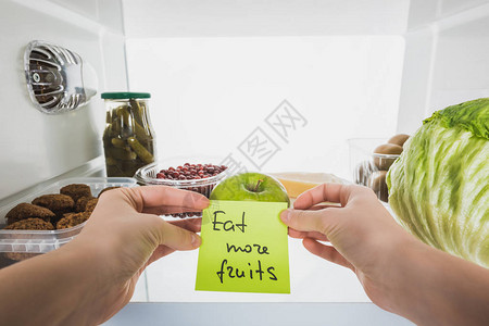 持有卡片多吃水果和在冰箱里以餐具背景与白色隔绝的白图片