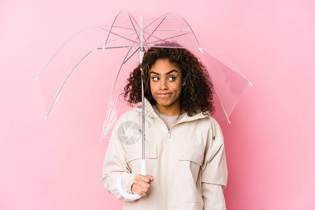 年轻美裔女子拿着伞子感到困惑疑惑和不确定图片