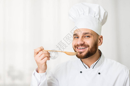 快乐的厨师人品尝食物拿着勺子微笑着站在厨房的窗户图片