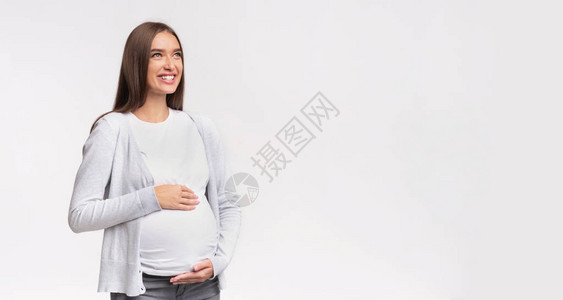 快乐怀孕微笑的孕妇摸着肚子看着一边站在白色的工作室背景空旷图片