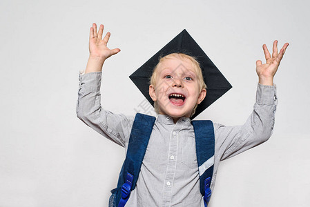一个带着学术帽子和书包的快乐金发男孩的肖像举起图片