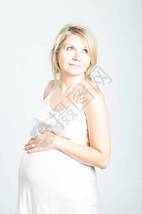 孕妇在白色睡衣触摸腹部的肖像图片