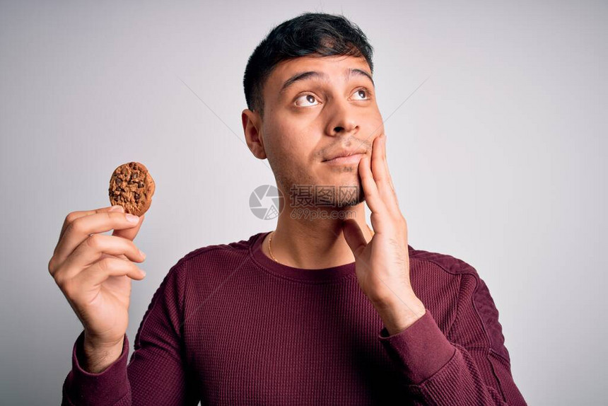 年青的西班牙人吃巧克力薯片饼干在孤立的背景下严肃地面对现实思考问题图片