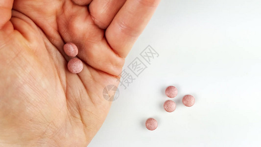 粉色药片在手掌和白色背景桌上的特写图片