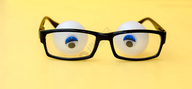 黄色背景上的黑色眼镜框眼镜后面是带有胶水瞳孔的网球概念眼镜后的眼睛图片