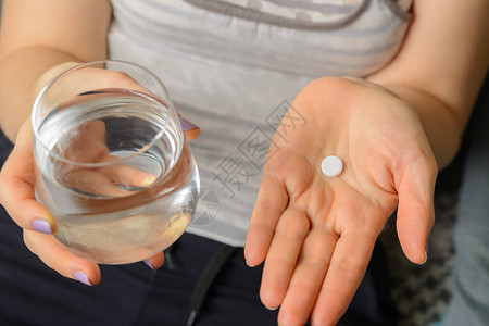 医用药片放在手掌中手握一杯水可以冲洗图片