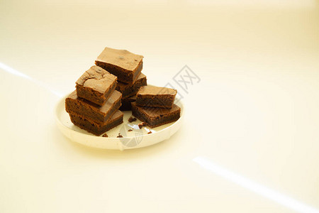 在干净的白色背景上堆放在白盘子里的方形巧克力蛋糕美味的巧克力早图片