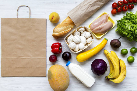 白色木制背景上的健康生食纸袋烹饪食物背景新鲜水果蔬菜鸡胸肉顶视图的平图片
