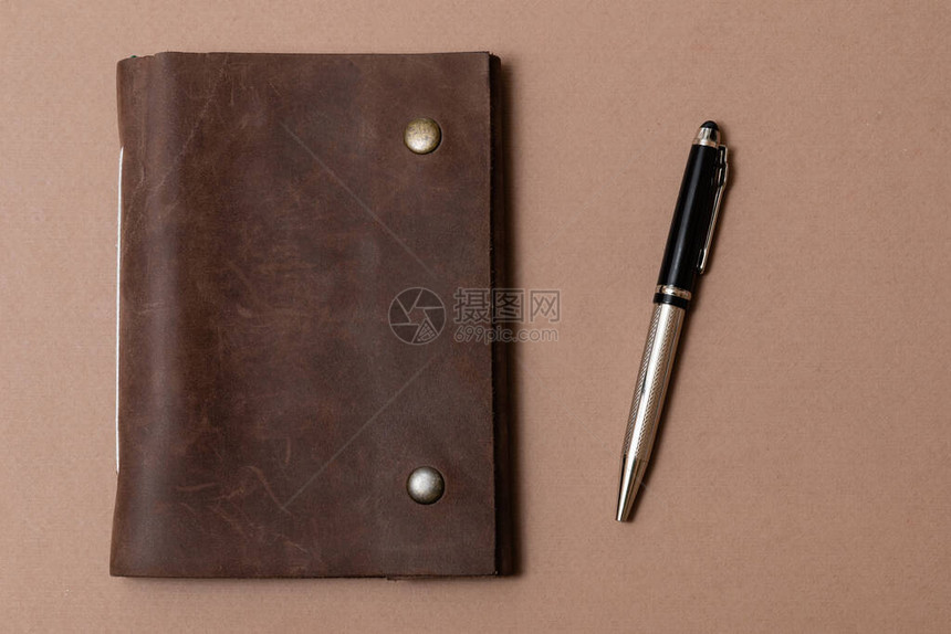 棕色背景上的复古皮革笔记本和铅笔图片