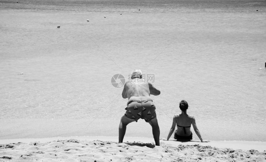 漫画和有趣的景象一个老人拍了坐在沙滩上的漂亮女孩的背影照图片