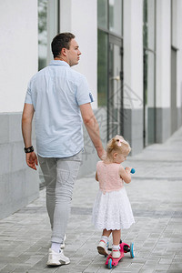 父亲和女儿在街上牵着手走一个金发的马尾巴女孩骑着摩托背景图片