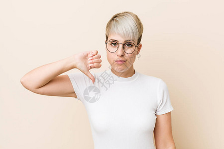 穿着白衬衫的年轻纯正自然女人表现了不喜欢的手势拇指低落背景图片