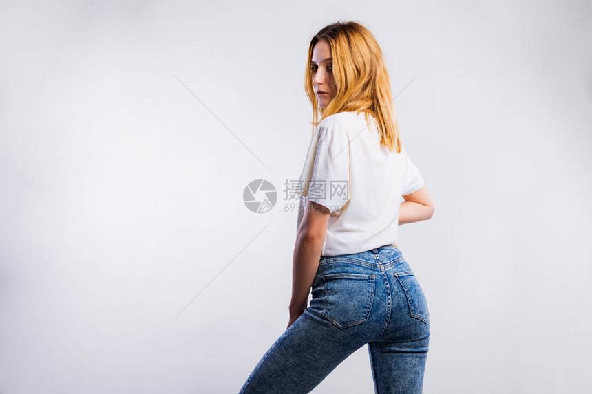 一个穿着牛仔裤和灰色背面空白T恤的有吸引力的年轻女子图片
