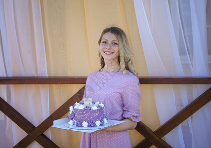 穿紫色裙子的年轻漂亮女孩拿着15号生日蛋糕配着紫奶油和图片