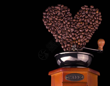 心形的咖啡豆被倒入一个黑色背景的咖啡研磨机图片