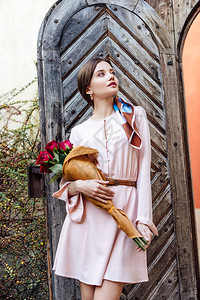 女孩抱着红玫瑰花束站在旧木门旁看不图片