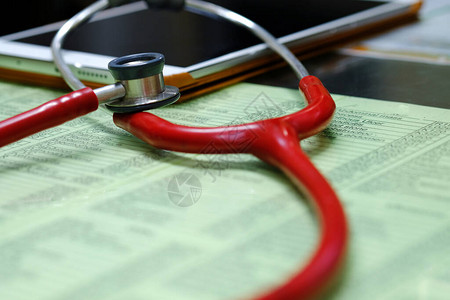 典型医生办公桌上的红色听诊器和平板电脑背景图片