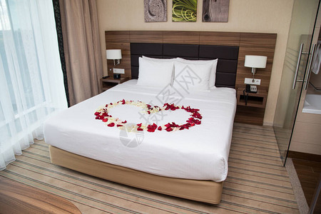 酒店床铺有红玫瑰花瓣的照片背景图片