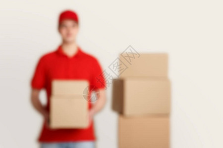 身穿红色制服持有包裹靠近堆叠箱的邮递图片