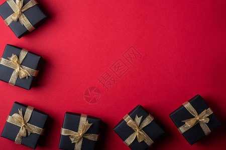 红纸框边背景上带金丝带的黑色礼盒图片
