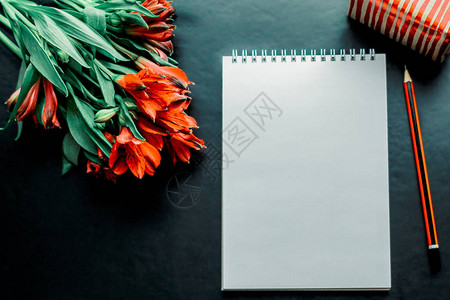 桌子笔记本铅笔和一束红花深背景图片