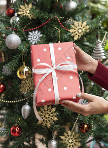 妇女手拿着红色礼物盒在圣诞树背景为圣诞图片