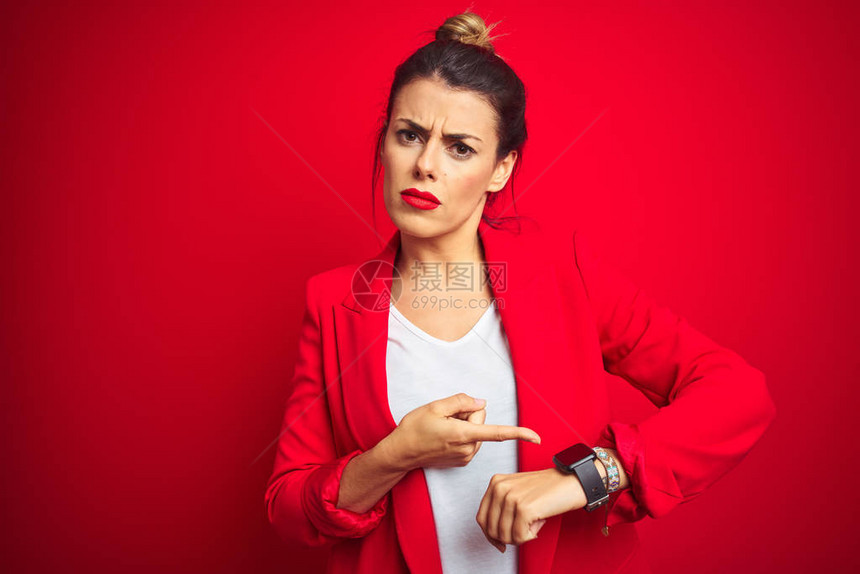 站在红色孤立背景上的年轻漂亮女商人急忙指点看时间不耐烦心烦意乱和愤怒图片