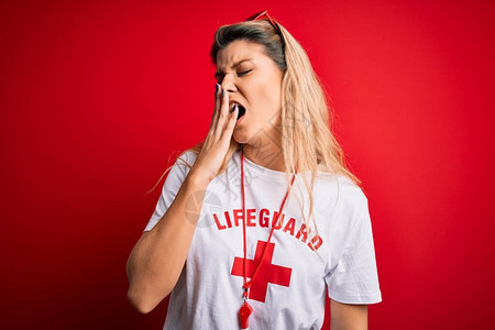 年轻漂亮的金发救生员女人穿着t恤与红十字和口哨无聊打哈欠累用手捂嘴图片