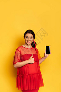穿着红色装扮的孕妇在黄色上用空白屏幕挂着智能手机图片