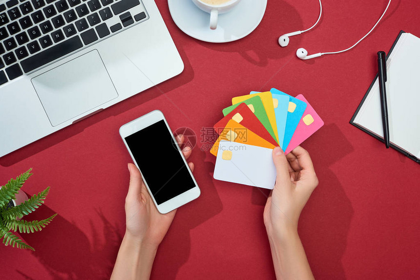 女手持彩色空信用卡和红色背景智能手机笔记本电脑耳机图片