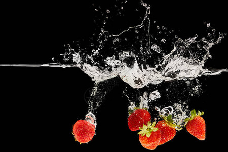 新鲜成熟的草莓落入水中溅起黑色的水花背景图片