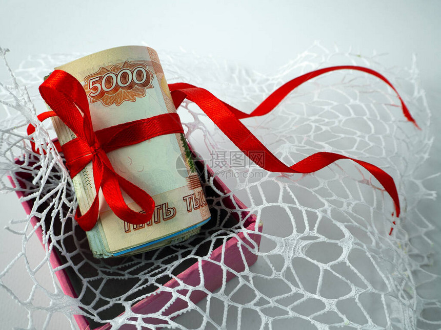 俄罗斯卢布钞票卷起并用红丝带系住钱放在粉红色盒子里的镂空织物表面上与俄罗斯卢图片