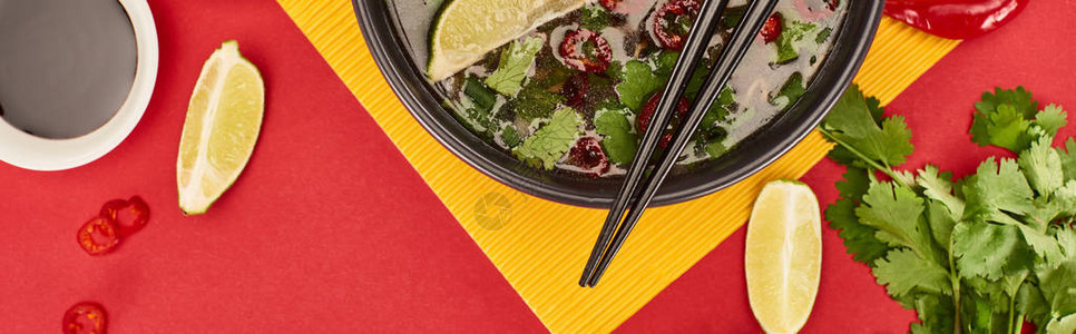 碗里有竹棍的Pho在红和黄色背景的酱油石灰辣椒和coriader附图片