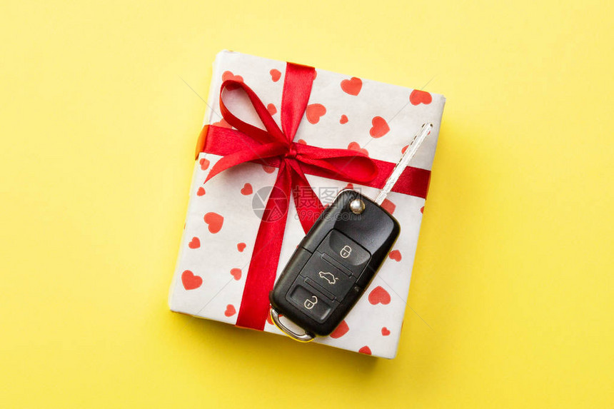 给礼品车钥匙概念顶视图在黄色背景上带有红丝带蝴蝶结心形和车图片