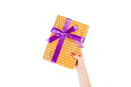 女人的手用紫色丝带用橙色纸包着圣诞或其他节日手工礼物图片