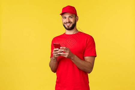 非接触式支付在线交付网上购物和包裹跟踪概念身穿红色制服帽T恤使用手机和相机黄色背景的背景图片
