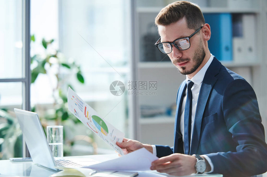 深重的年轻经济学家在眼镜和正式服装中按工作场所分列通过财务文件图片